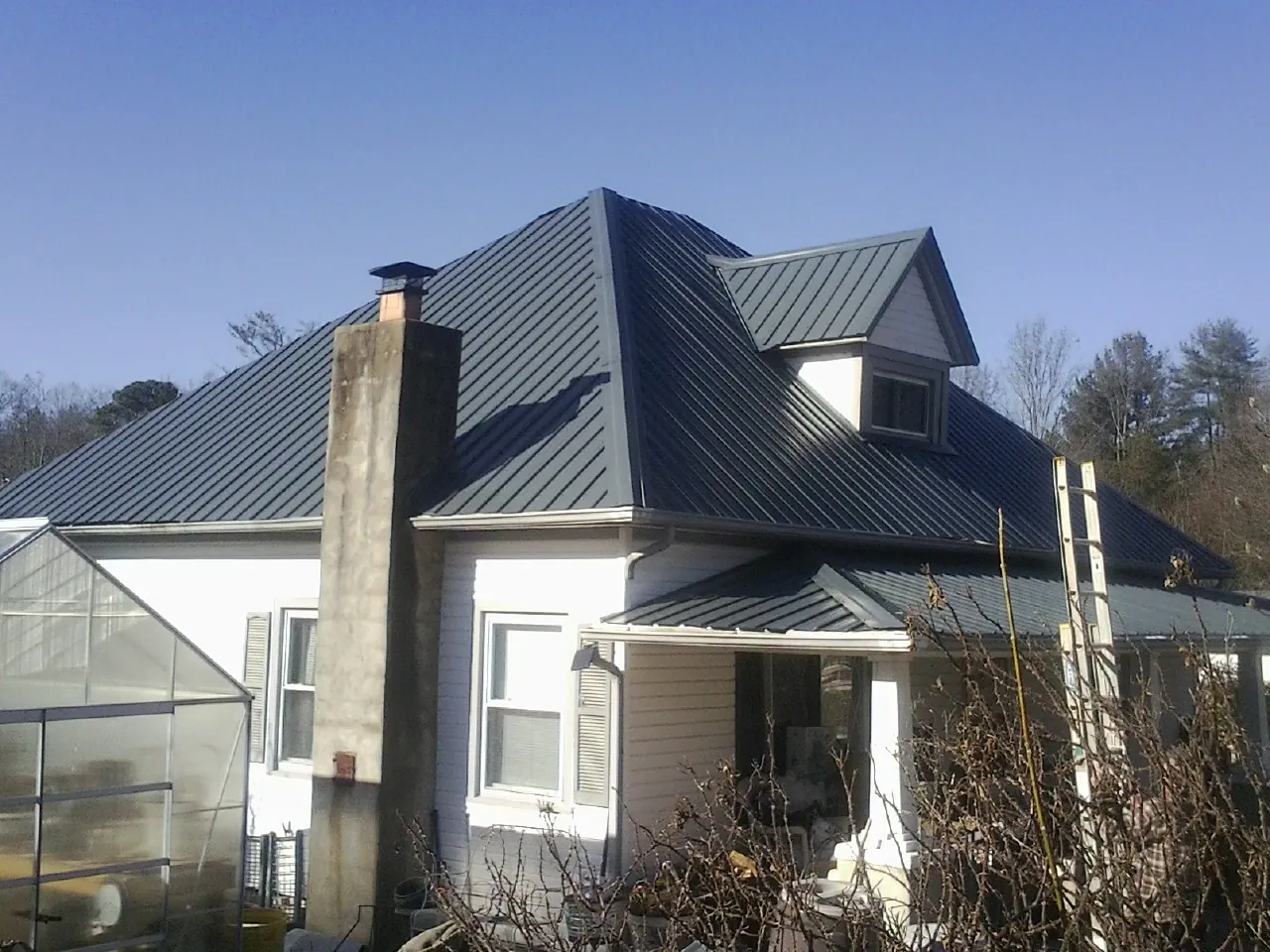 Dark blue standing seam metal roof on a white farmhouse with dormer — Slate & Tile Roof Repair by Roofing Brothers in Rimforest