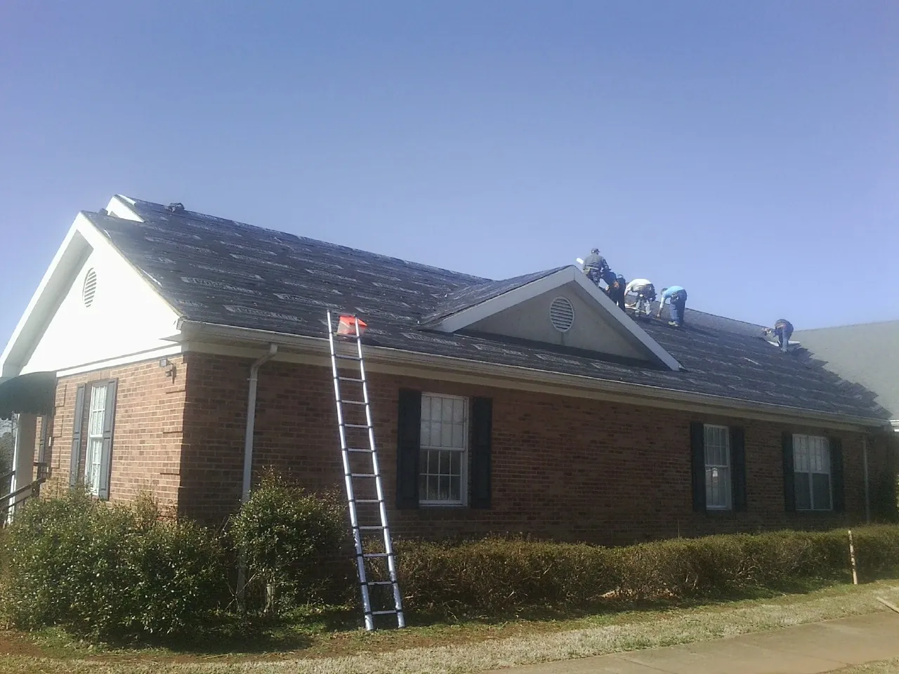 Crew tearing shingles off a brick ranch roof with a ladder set — Metal Roof Repair work by our crew in Rimforest