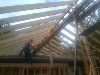 Rafters going up over a new addition with a worker on the wall in Rimforest