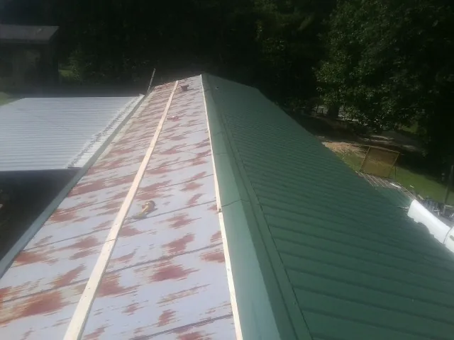 Old rusted panels beside newly installed green metal roofing — Wind Damage Roof Repair by Roofing Brothers in Rimforest