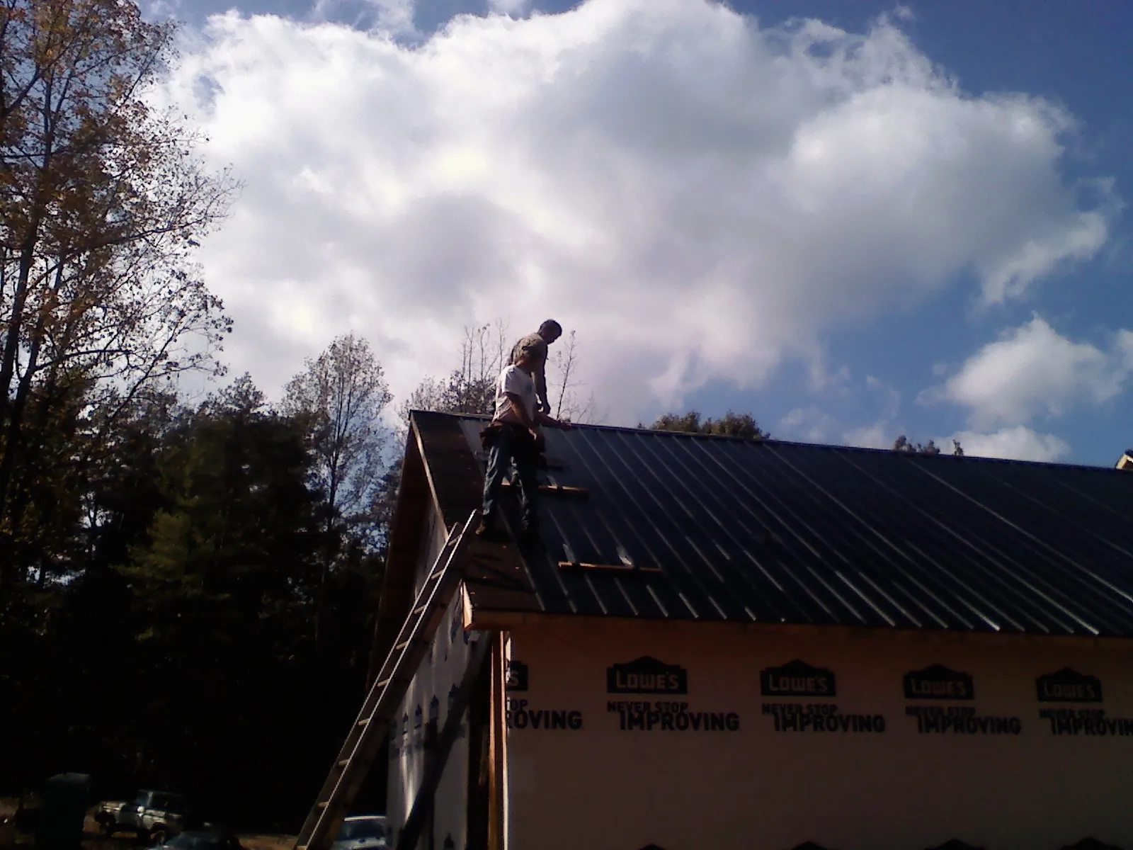 Roofer fastening dark metal panels high against a cloudy sky, from a Roof Inspection job in Rimforest