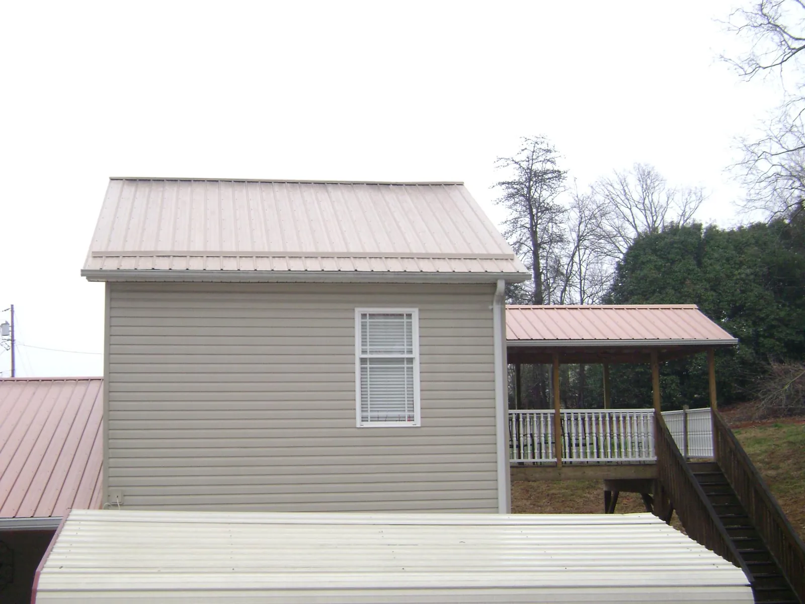 Tan metal roofs on a two story addition and attached porch, from a Roof Replacement job in Rimforest
